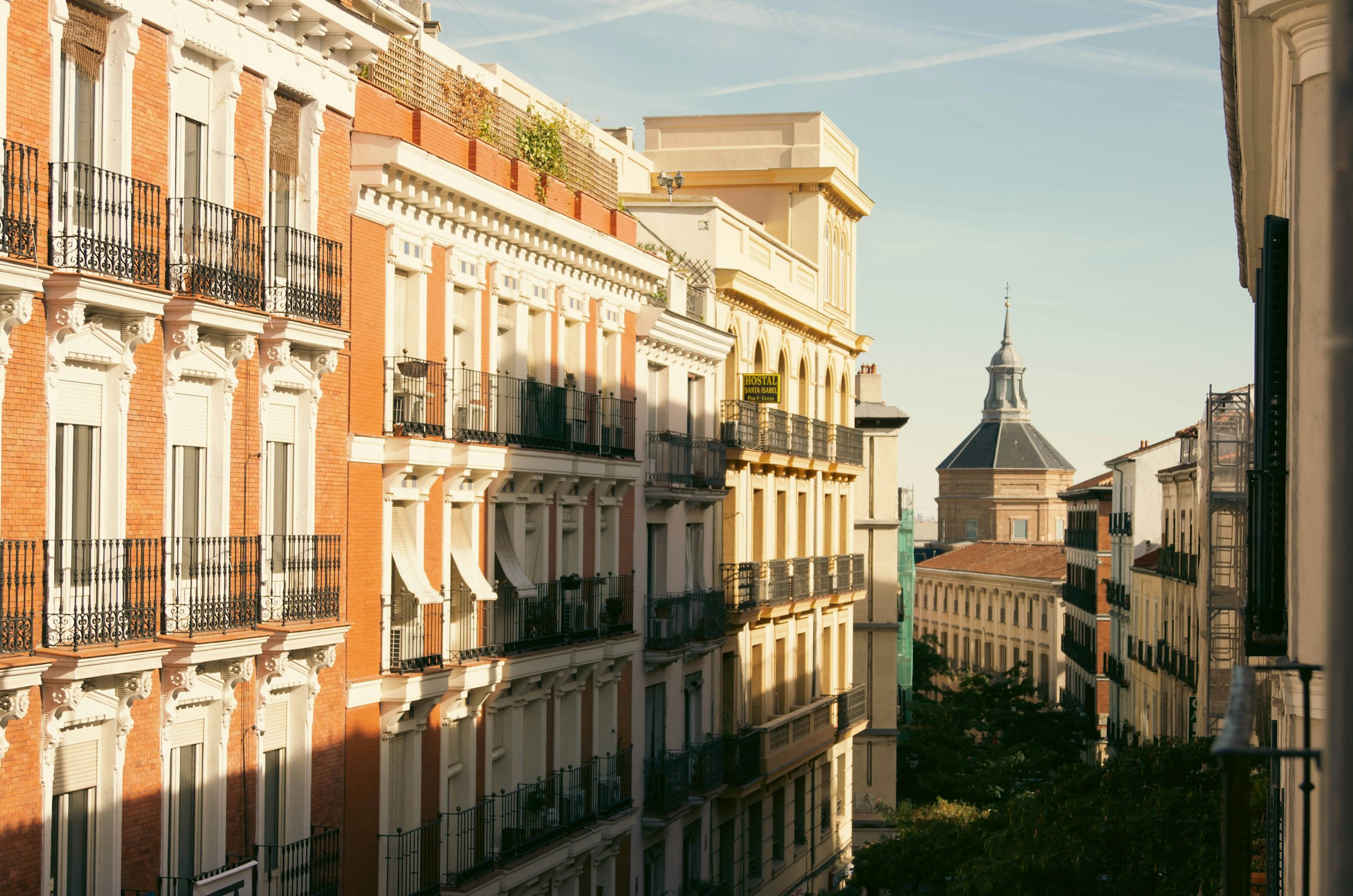 Fachadas ocre con balcones y una cúpula al fondo, Madrid